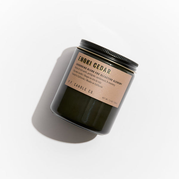 P.F. Candle Co. EU Enoki Cedar Alchemy Candle - Product - Alchemy Candles feature smoke-colored glass vessels, black metal lids, and gold-leafed labels inspired by vintage window lettering.